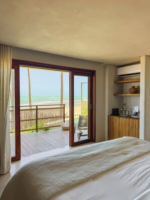 A bedroom with a large bed, a wooden desk, and a view of the beach.