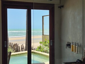 A bathroom with a view of a beach and ocean through a glass door.