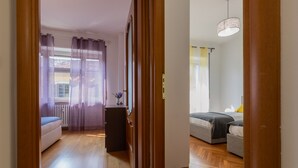 A hallway leading to a bedroom with a bed, a dresser, and a window with curtains. - San Domenico Family Flat by Wonderful Italy (Turin)