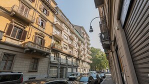 A narrow street lined with parked cars and multi-story buildings with balconies and shutters. - San Domenico Family Flat by Wonderful Italy (Turin)