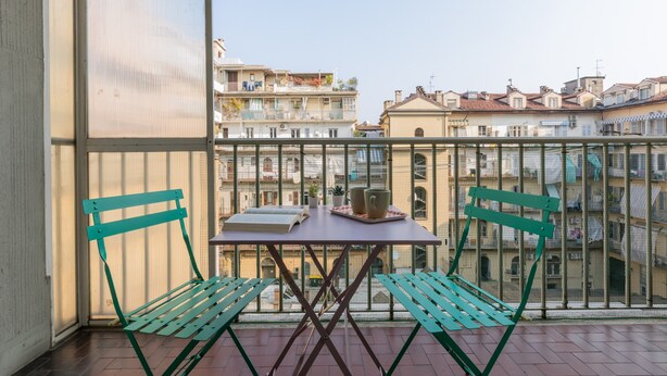 A balcony with a table and two chairs, overlooking a cityscape with buildings. - San Domenico Family Flat by Wonderful Italy (Turin)