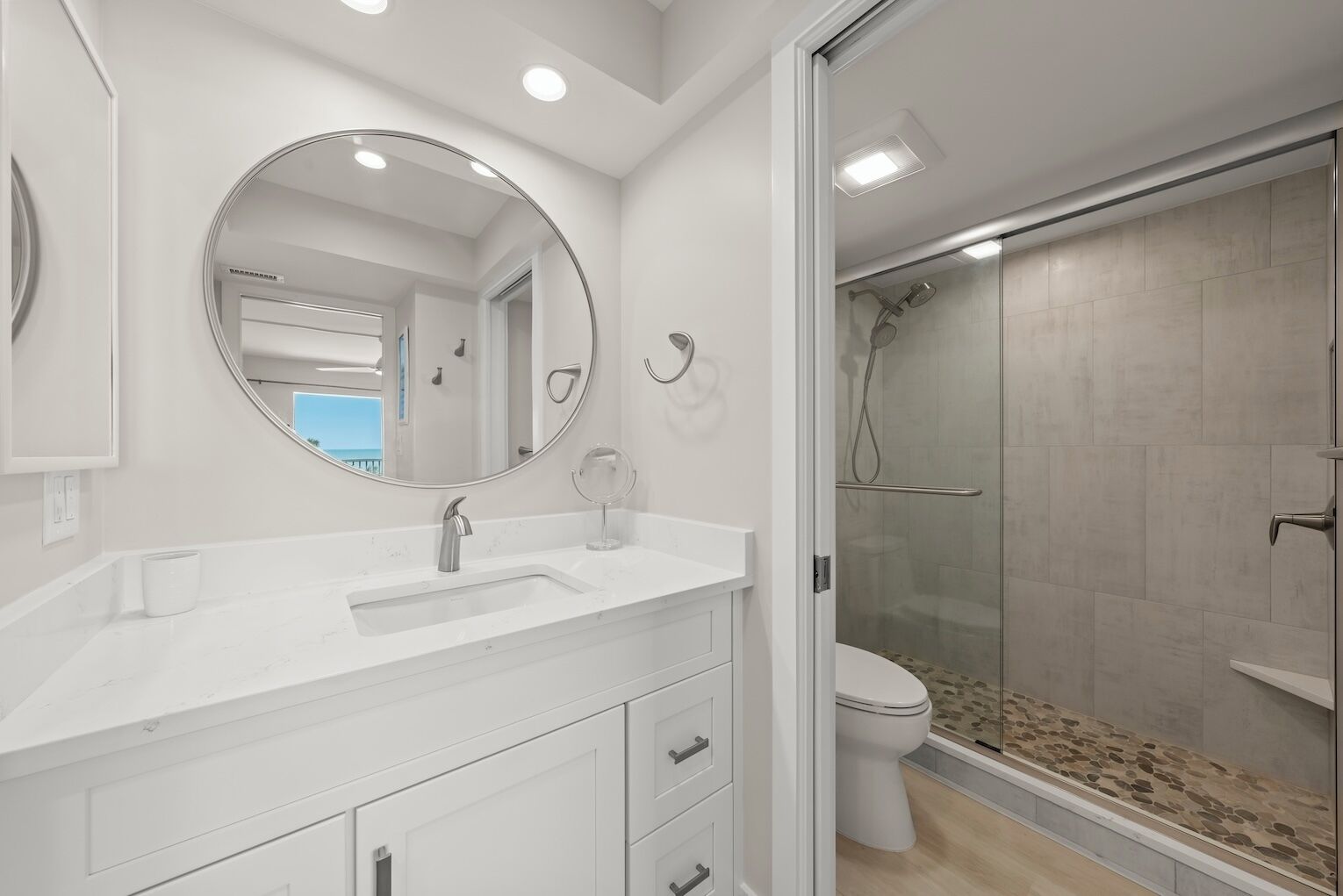 Une salle de bain moderne avec un grand miroir rond, un lavabo blanc et une douche à parois de verre.