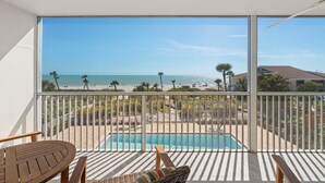 En balkon med udsigt over en strand, en pool og en bygning i baggrunden.