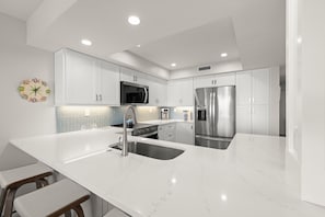 Une cuisine moderne avec des meubles blancs, des appareils en acier inoxydable, un plan de travail en marbre et un évier encastré.