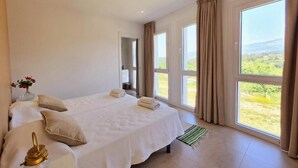 A bedroom with two beds, large windows, a view of greenery, and a bathroom visible through an open door. - The tranquility of the mountain near the Miño river. (ARBO)