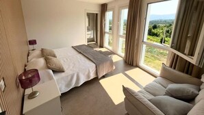 A spacious bedroom with a large bed, a sofa, and a view of a lush landscape through the windows. - The tranquility of the mountain near the Miño river. (ARBO)