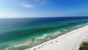 Una playa con aguas turquesas cristalinas, una orilla arenosa y un muelle que se adentra en el mar.
