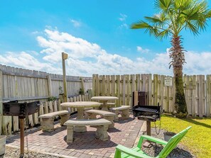 A patio area with a wooden fence, a palm tree, a barbecue grill, and outdoor seating.