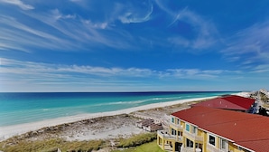 A beachfront property with a red-roofed building, a sandy beach, and a clear blue sky. - Regency Towers #707 West | Sunset Views, Pool, Tennis/Pickleball (Pensacola Beach)
