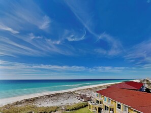 A beachfront property with a red-roofed building, a sandy beach, and a clear blue sky.