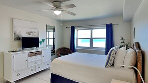 A bedroom with a bed, a dresser, a television, and a window with curtains. - Regency Towers #707 West | Sunset Views, Pool, Tennis/Pickleball (Pensacola Beach)