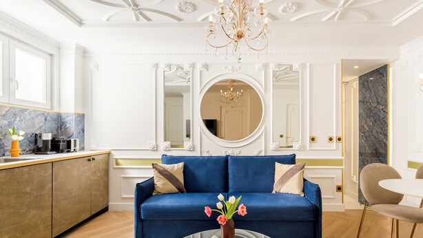 A modern living room with a blue sofa, a glass coffee table, and a chandelier.