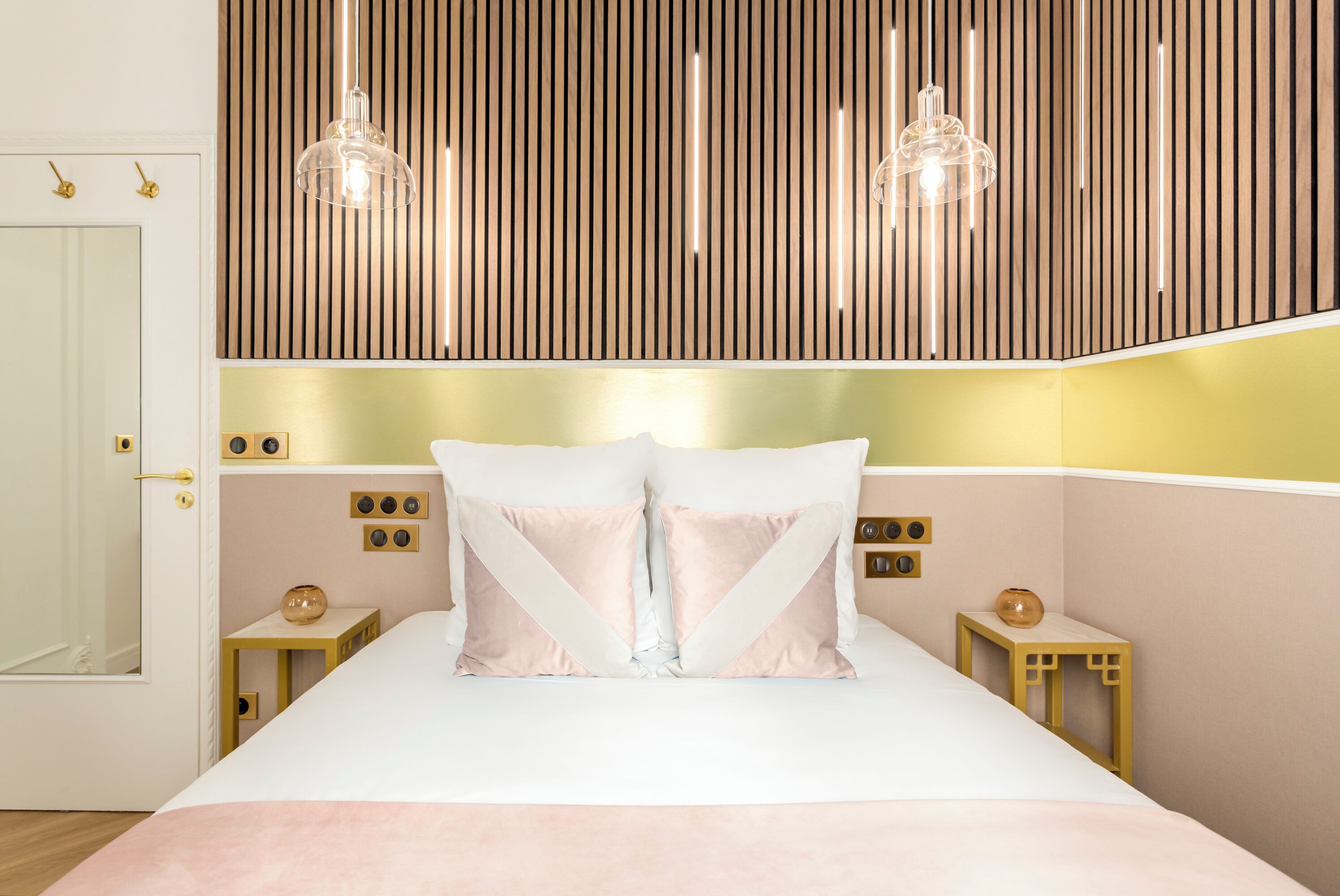 A modern bedroom with a large bed, two bedside tables, a wooden slat wall, and pendant lighting.