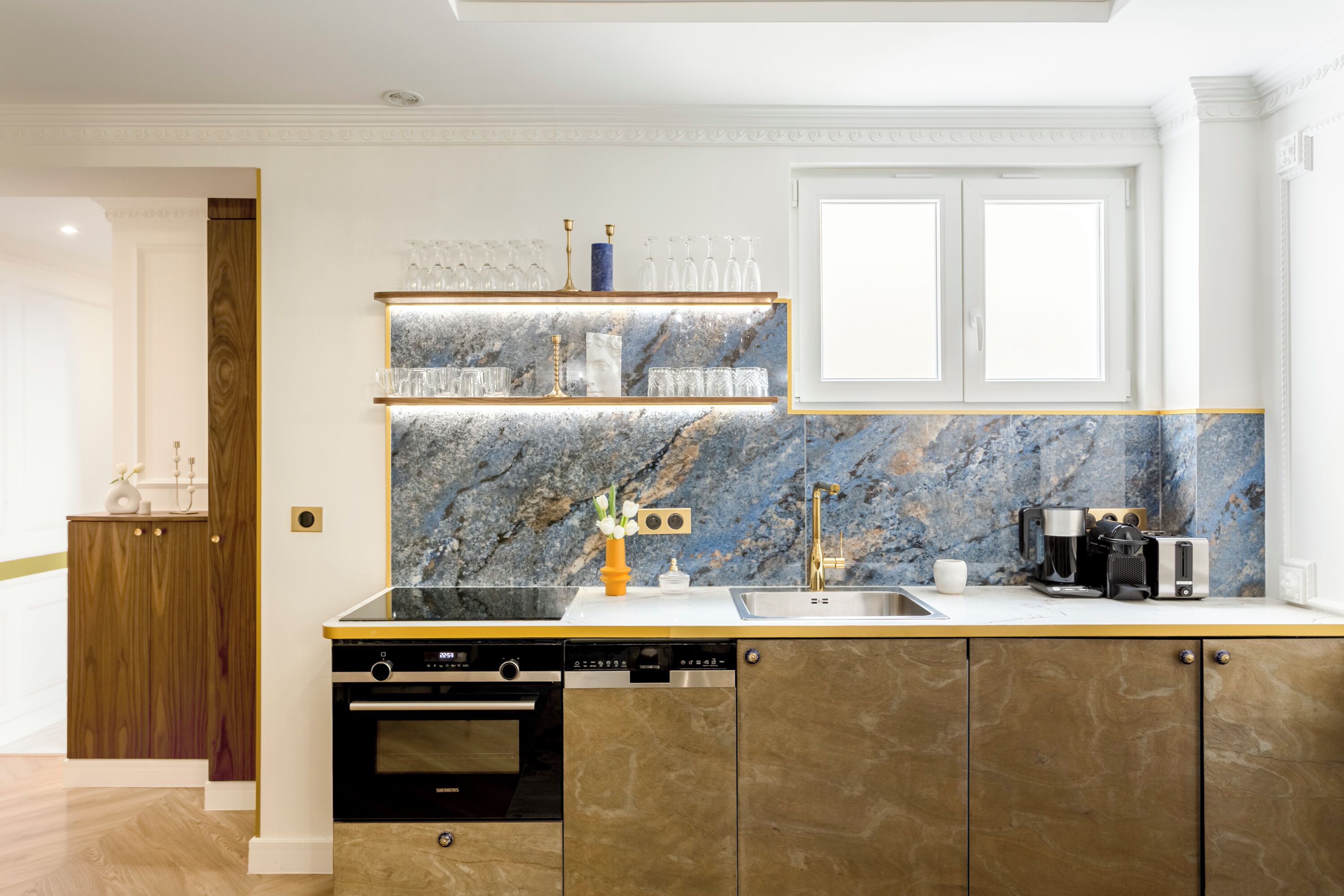 A modern kitchen with marble backsplash, built-in oven, and stainless steel appliances.