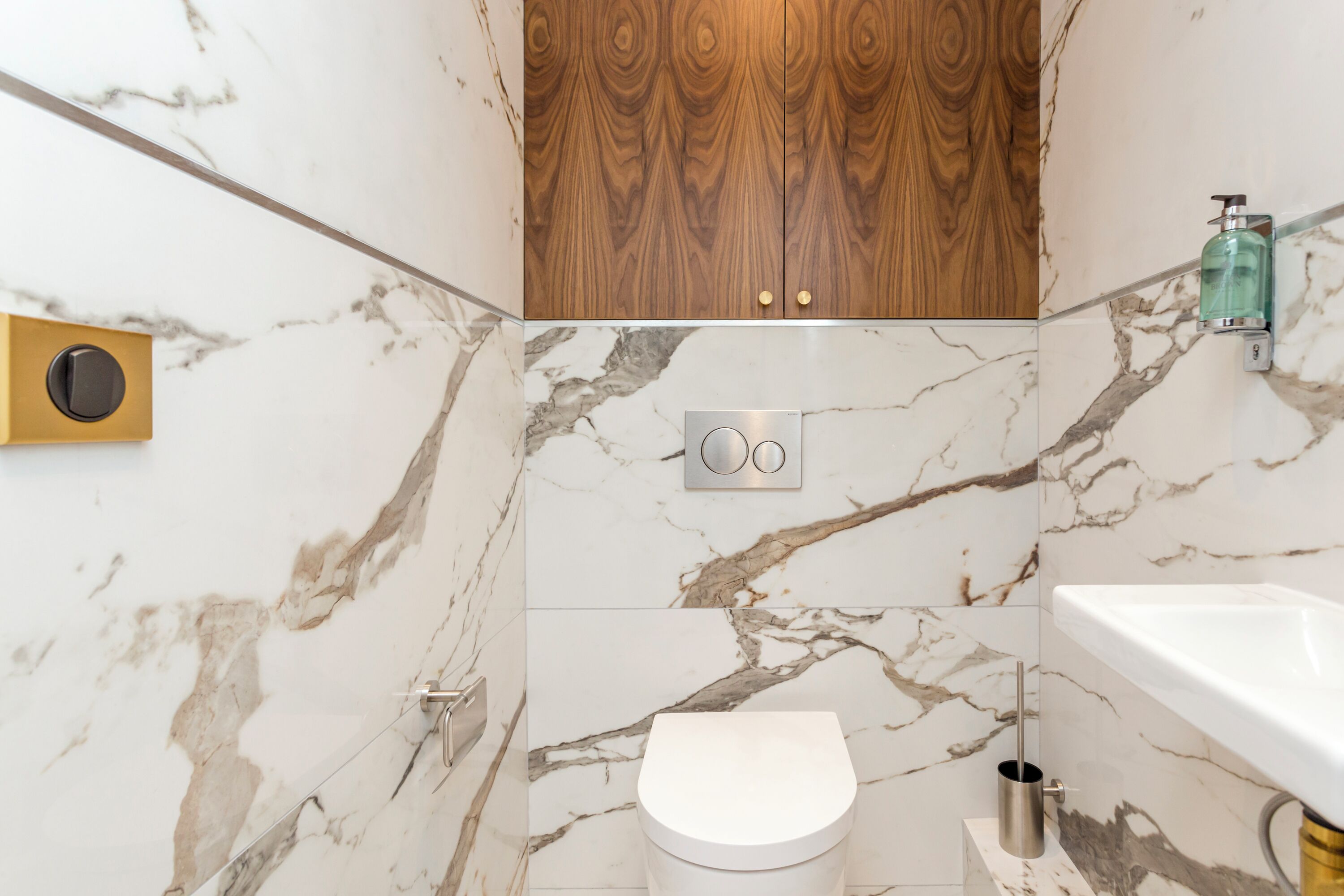 A bathroom with a marble floor, a white toilet, a wooden cabinet, and a white sink.