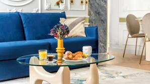 A modern living room with a blue sofa, a glass coffee table with breakfast items, and a decorative vase.