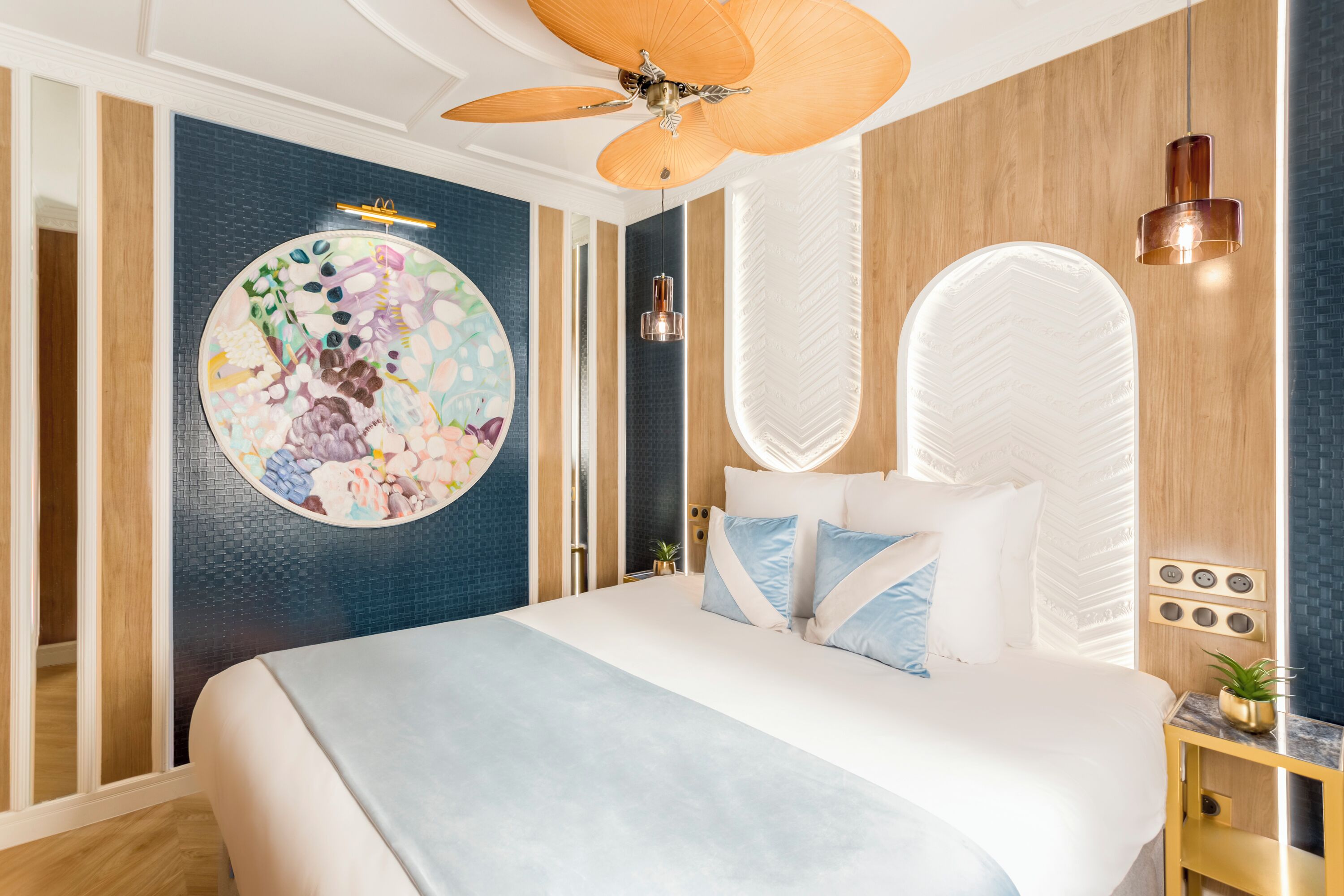 A modern bedroom with a large bed, a ceiling fan, a wall-mounted light fixture, and a decorative circular artwork.