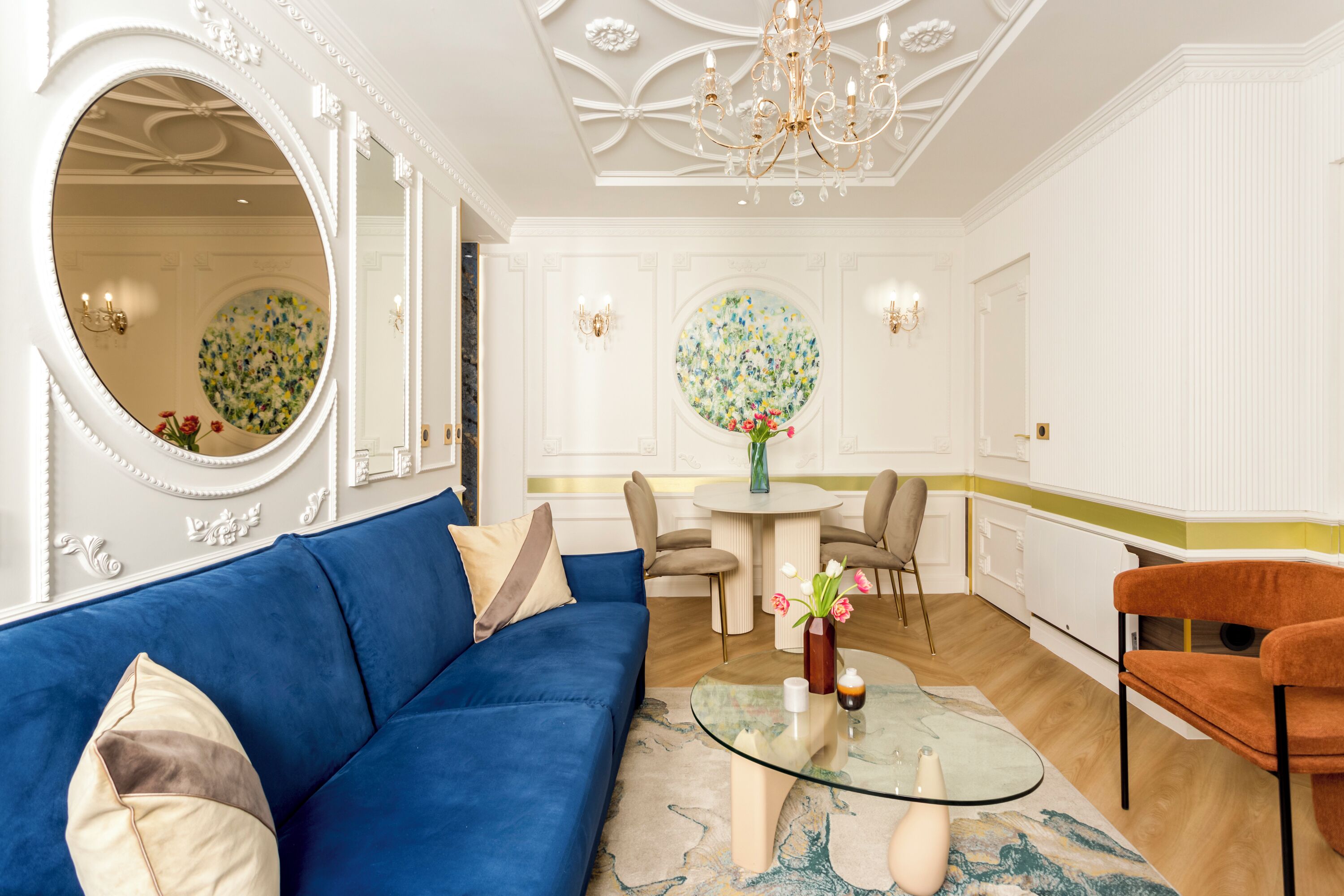 A modern living room with a blue sofa, a glass coffee table, and a round mirror.