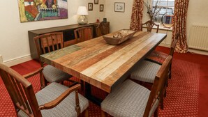 A dining room with a wooden table, patterned chairs, a bowl of fruit, and a cityscape painting on the wall.
