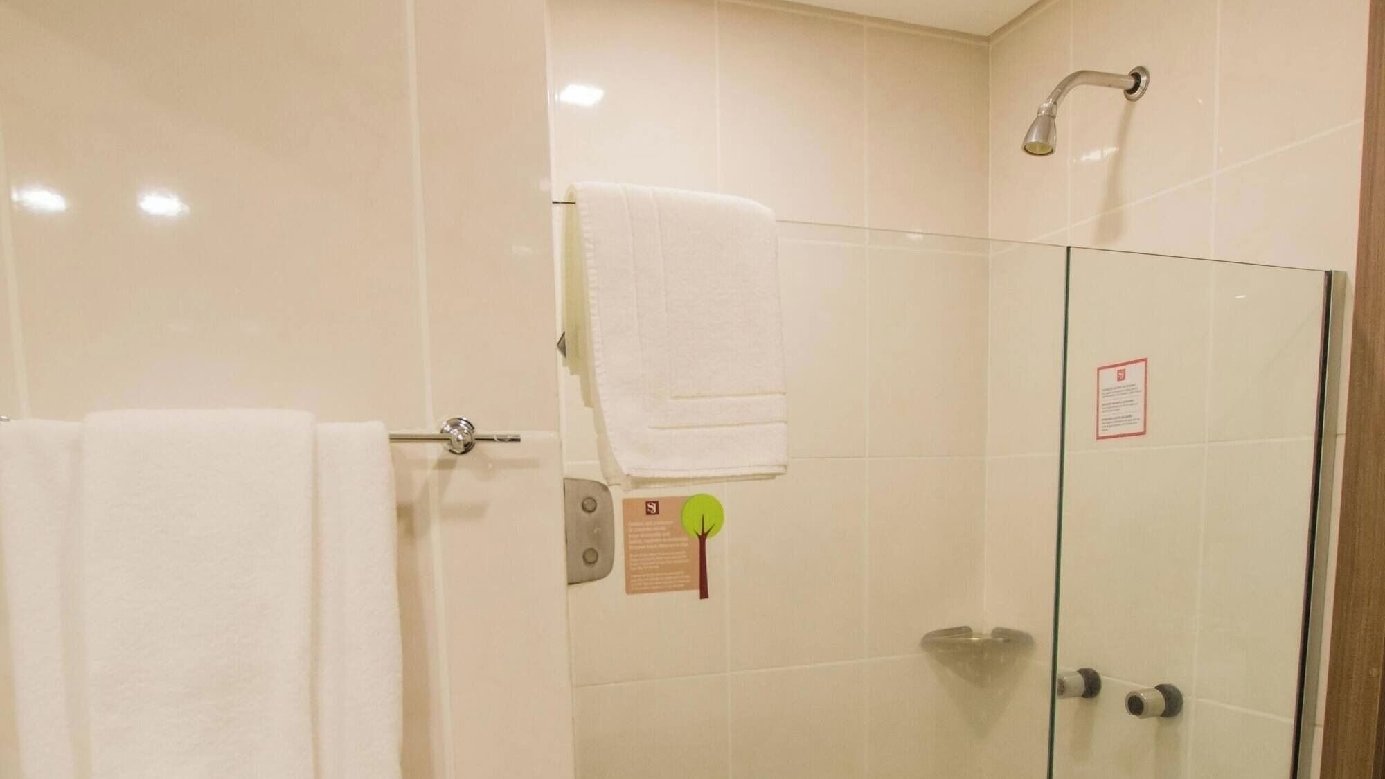 A bathroom with a glass shower enclosure, a towel rack with a white towel, and a safety sign on the wall.
