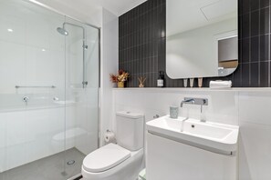 A modern bathroom with a glass-enclosed shower, a white toilet, and a sink with a mirror above it. - Collingwood Cool 2-bed, Balcony, Gym, Rooftop (Melbourne)