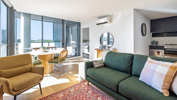 A modern living room with a green sofa, a patterned rug, and a dining area with a round table and chairs. - Collingwood Cool 2-bed, Balcony, Gym, Rooftop (Melbourne)