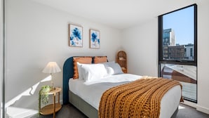 A modern bedroom with a large bed, a bedside table with a lamp, and two framed artworks on the wall. - Collingwood Cool 2-bed, Balcony, Gym, Rooftop (Melbourne)