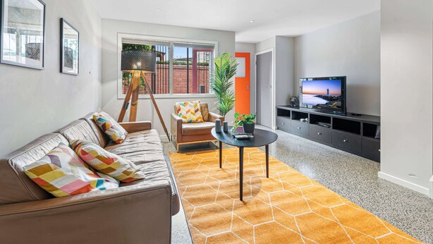 A modern living room with a sofa, a coffee table, a TV, and a staircase leading to an outdoor area. - Convenient Bayside Living at the Edge of the City (Melbourne)
