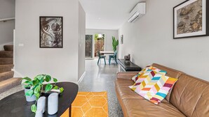 A modern living room with a brown leather sofa, a colorful geometric pillow, and a black coffee table with a plant and salt shakers. - Convenient Bayside Living at the Edge of the City (Melbourne)