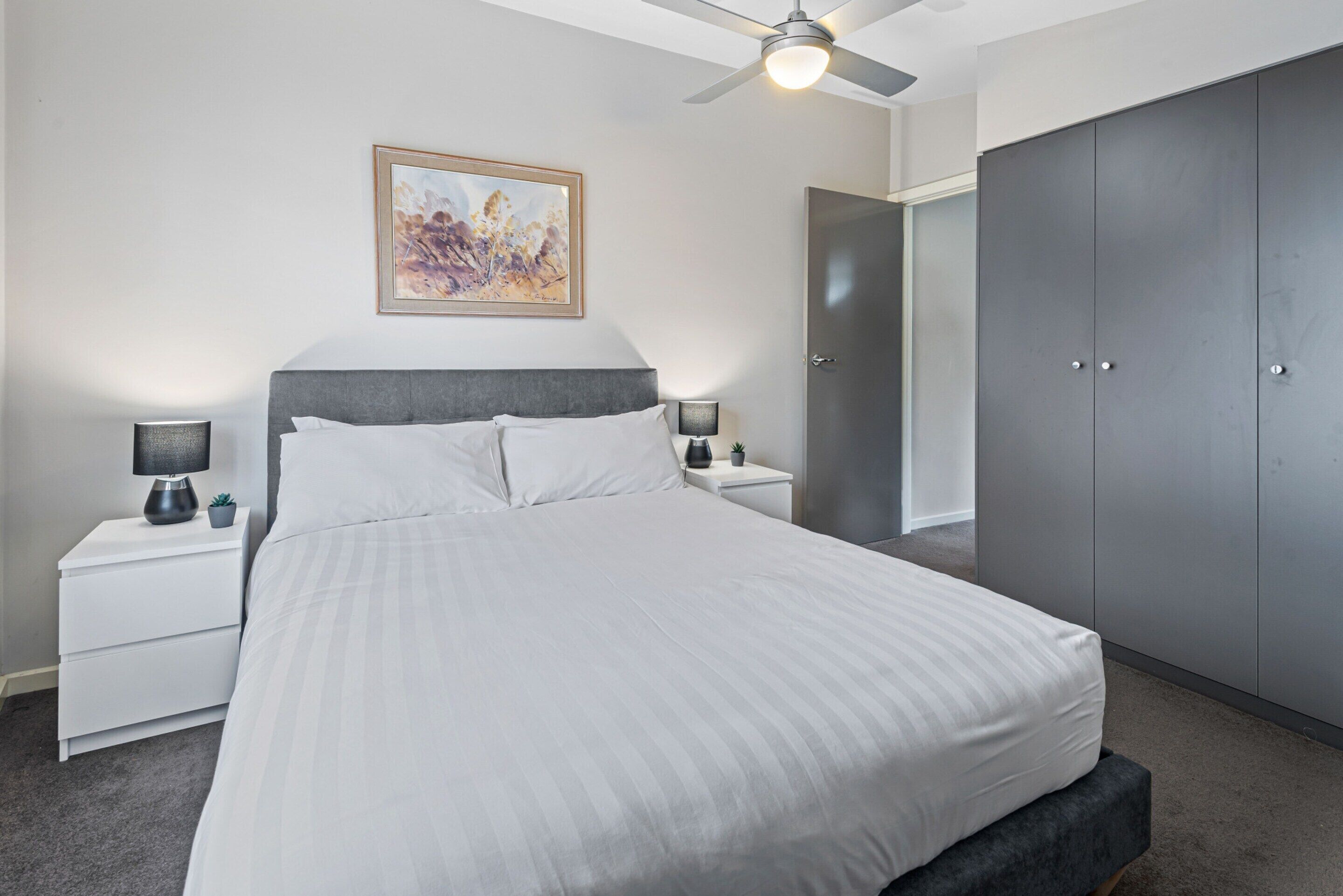 Camera da letto con un letto, comodini, una ventola a soffitto, un armadio e un quadro appeso al muro.