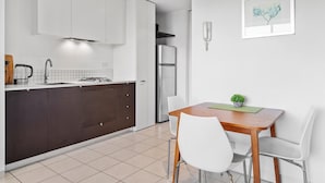A modern kitchen with white cabinets, a stainless steel refrigerator, and a dining area with a wooden table and white chairs. - Central 1-bed Apartment With Secure Parking (Melbourne)