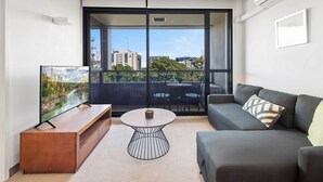 A modern living room with a sofa, a coffee table, and a TV on a wooden stand. - Central 1-bed Apartment With Secure Parking (Melbourne)