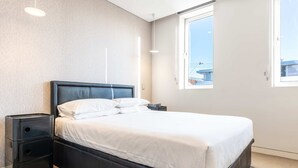 A neatly made bed with white linens in a modern room with a large window, a bedside table, and a wall-mounted light fixture. - Comfy 1-bed Apartment in Perfect Location (Sydney)