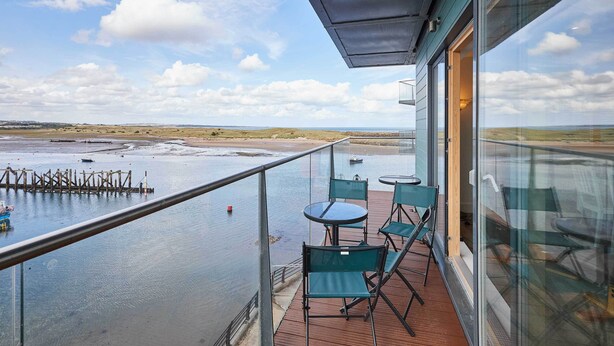 Un balcon avec vue sur une plage et la mer. On y trouve des chaises et une table.
