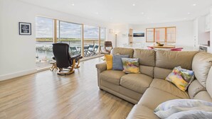 Un salon spacieux doté d’une grande fenêtre, d’un canapé beige et d’un coin repas avec une table et des chaises.