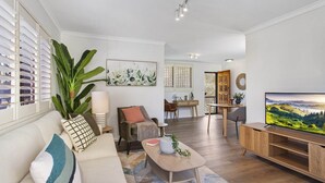 A modern living room with a sofa, coffee table, and TV stand. There is a dining area with a table and chairs in the background. - Cosy Unit With Parking Near New Farm Park & River (Brisbane)