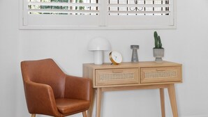A brown leather chair, a wooden side table with a white lamp, a clock, and two potted cacti. - Cosy Unit With Parking Near New Farm Park & River (Brisbane)