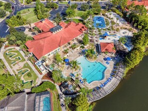 Eine Luftaufnahme eines Resorts mit einem großen Schwimmbad, Tennisplätzen und einem Parkplatz.