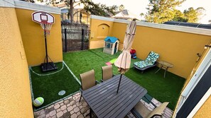 Ein Garten mit Kunstgrasanlage, einem Basketballkorb, einem kleinen Spielhäuschen und Gartenmöbeln.