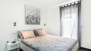 Et soveværelse med seng, sengeborde, vægmonteret lampe, et vindue med gardiner og et blomstermotiv.