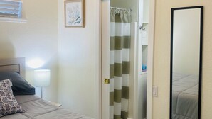 A bedroom with a bed, a ceiling fan, an air conditioning unit, a shower curtain, and a mirror.
