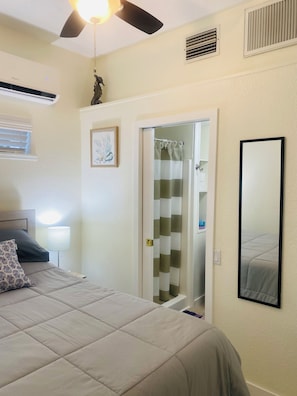 A bedroom with a bed, a ceiling fan, an air conditioning unit, a shower curtain, and a mirror.