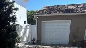 A residential driveway leading to a garage with a white door, surrounded by a white picket fence, potted plants, and a brick pathway.
