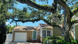 A single-story house with a garage, a front porch, and a large tree in front.