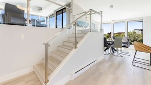 Un intérieur moderne avec un escalier, un coin repas et de grandes fenêtres.