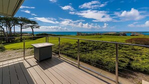 Une terrasse en bois avec une rambarde en métal, d’où l’on peut admirer un paysage verdoyant et la mer.