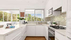 Une cuisine moderne avec des meubles blancs, une grande fenêtre et un pare-feu en carreaux.