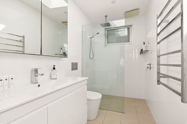 Un baño moderno con ducha de vidrio, tocador blanco con espejo y un inodoro.