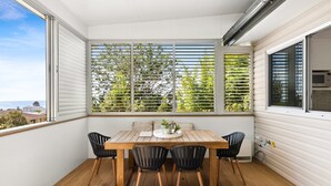 Un balcon avec une table et des chaises en bois, une vue sur la ville et une fenêtre avec des stores.