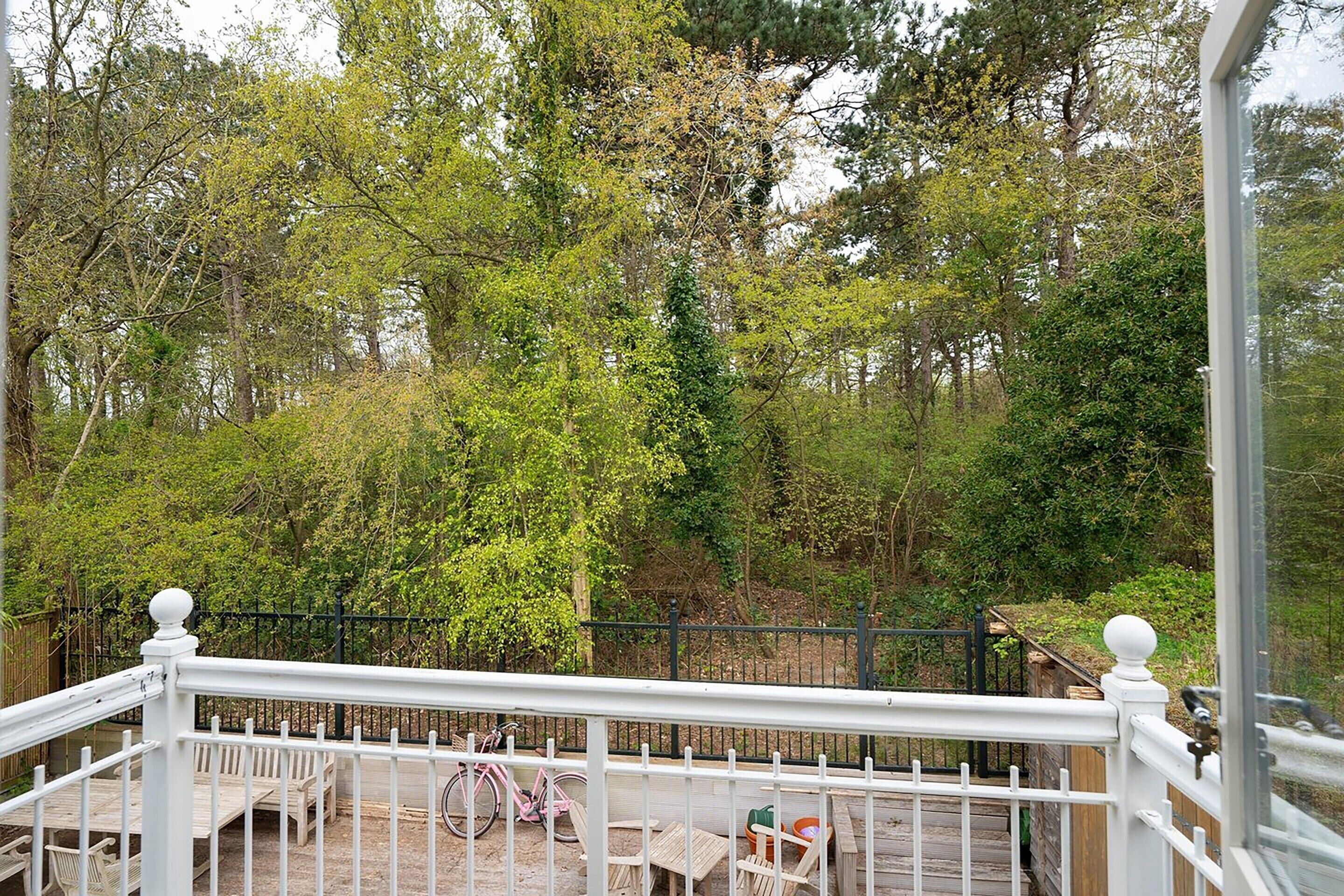 A wooden deck with outdoor furniture, surrounded by a white railing and a black fence.